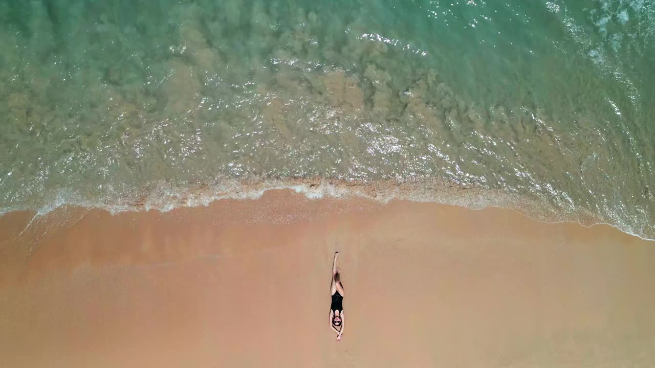 鸟瞰图，穿着红色衣服的女人在海滩上快乐地玩着海浪视频素材