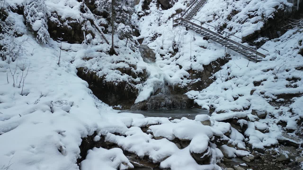 冬天在白雪皑皑的阿尔卑斯山上，白天在奈塞尔旺瀑布的树木和岩石上飞行视频素材