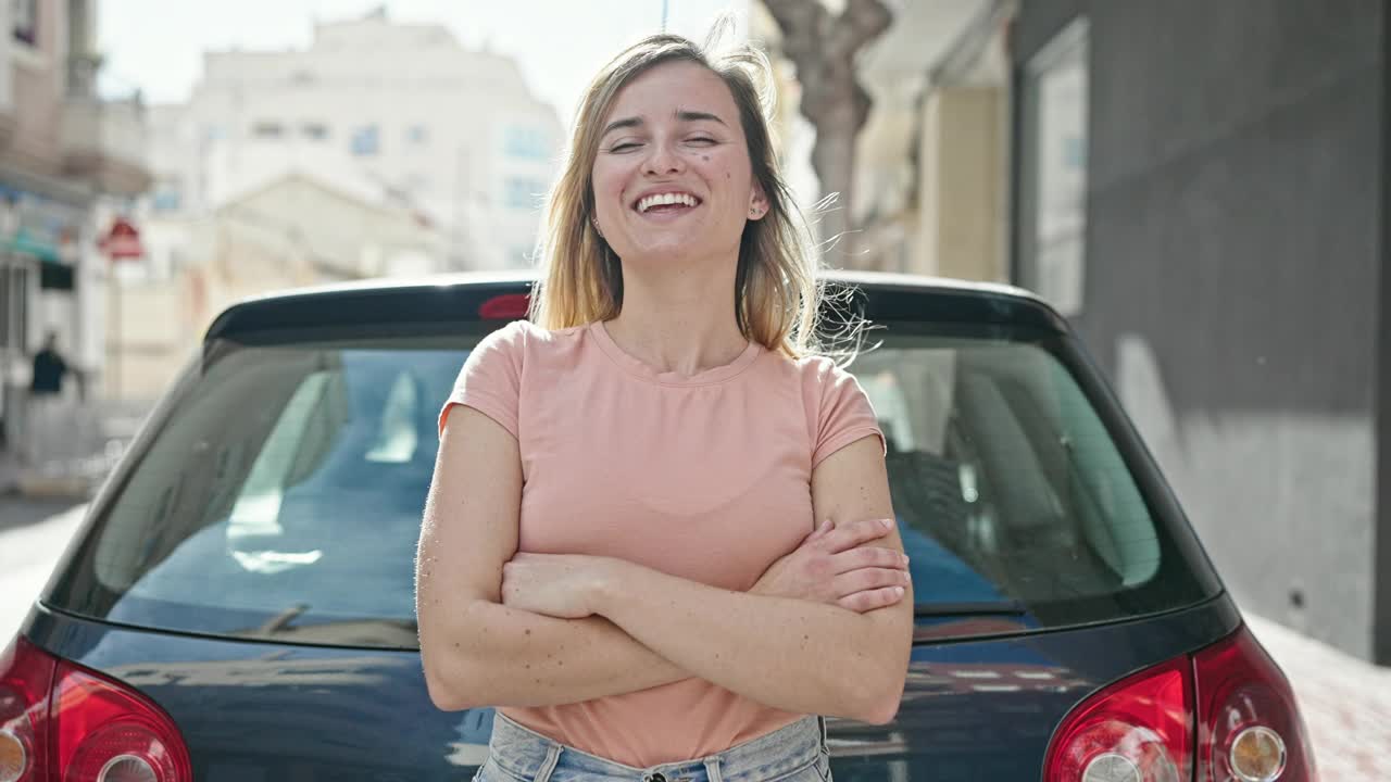 年轻的金发女子微笑自信地站在车旁，双手交叉在街上视频素材