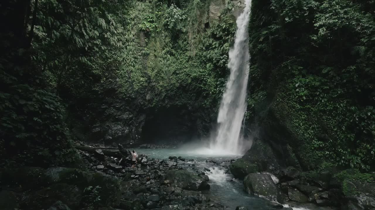 热带树木覆盖的落基山脉之间的瀑布航拍视频视频素材