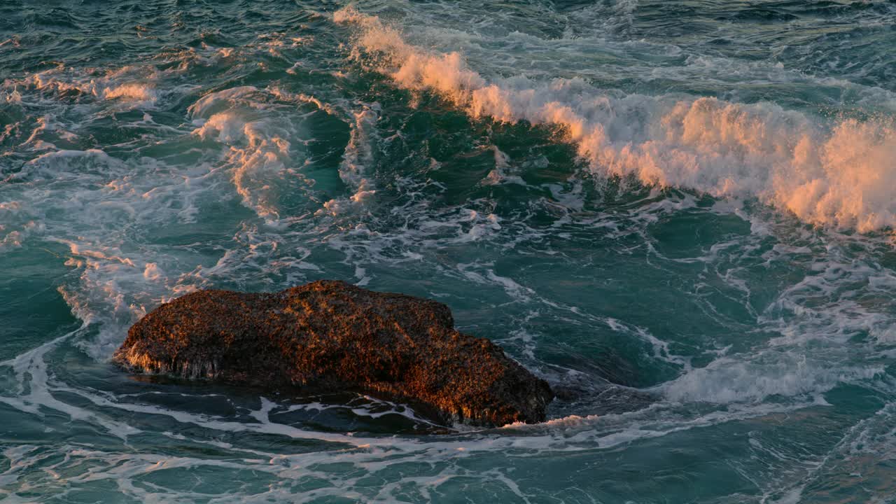 高浪翻滚黑暗的岩石在阳光下大自然近距离。海水破裂视频素材