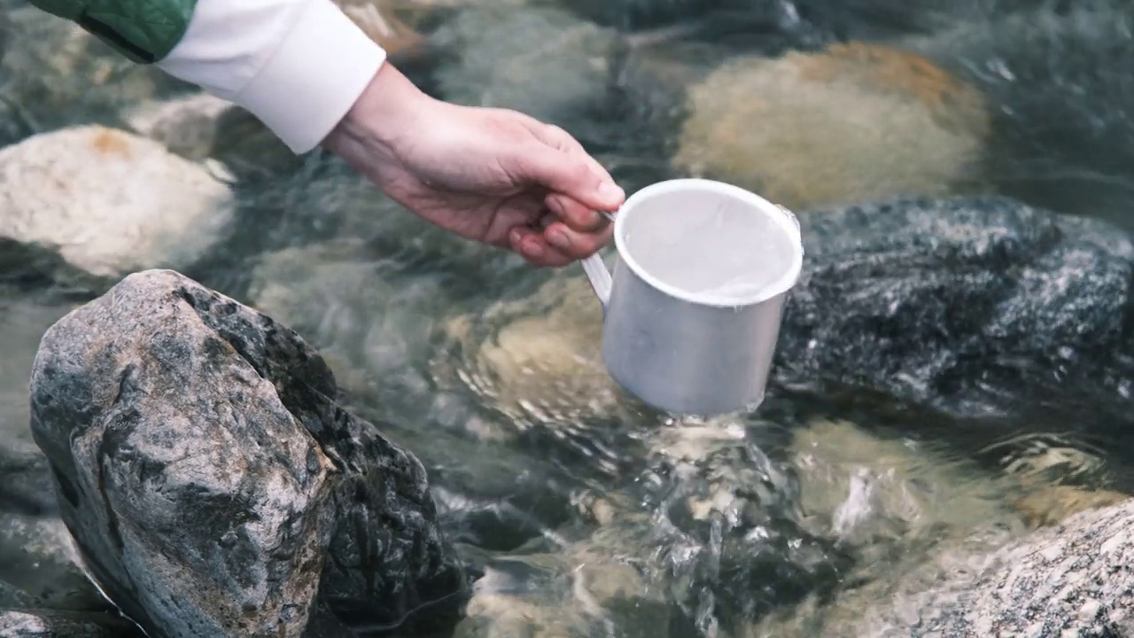 女背包客正拿着金属杯从山河中取水视频素材