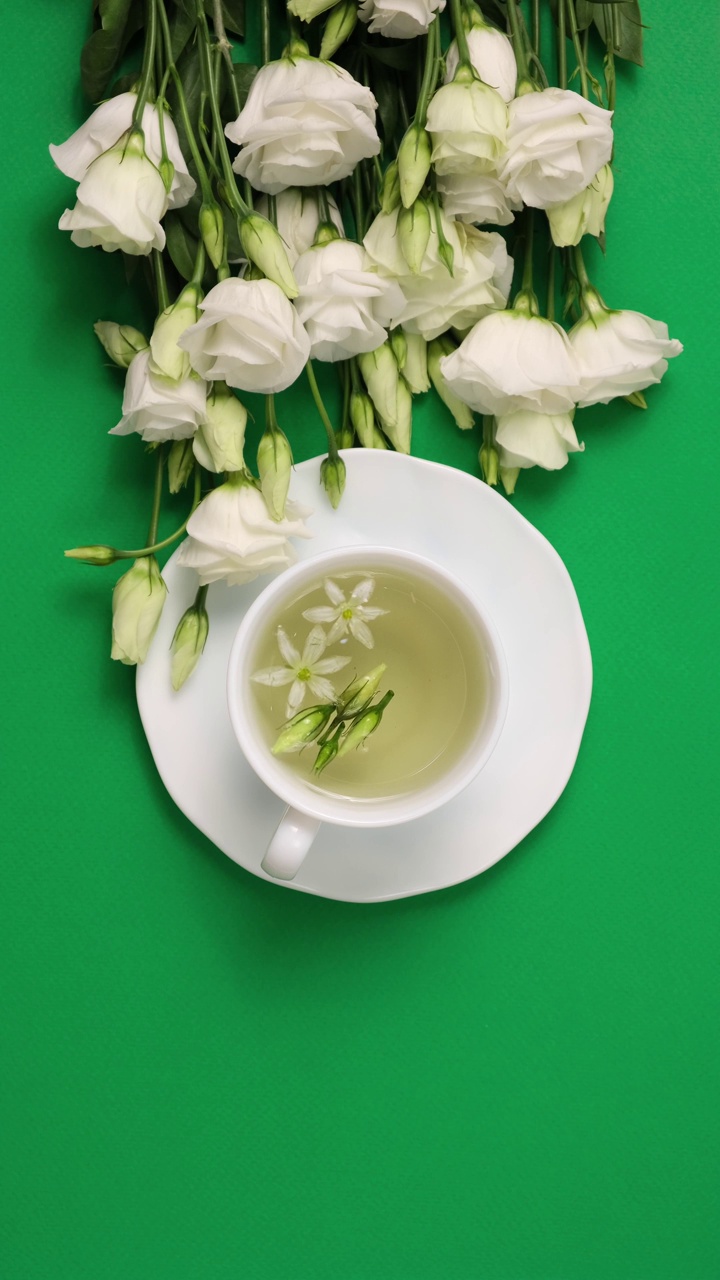 花卉茶。白色的杯子里有香浓的凉茶和百合花附近。下午茶时间。放松与花草茶，白色背景，顶视图，垂直视频视频素材