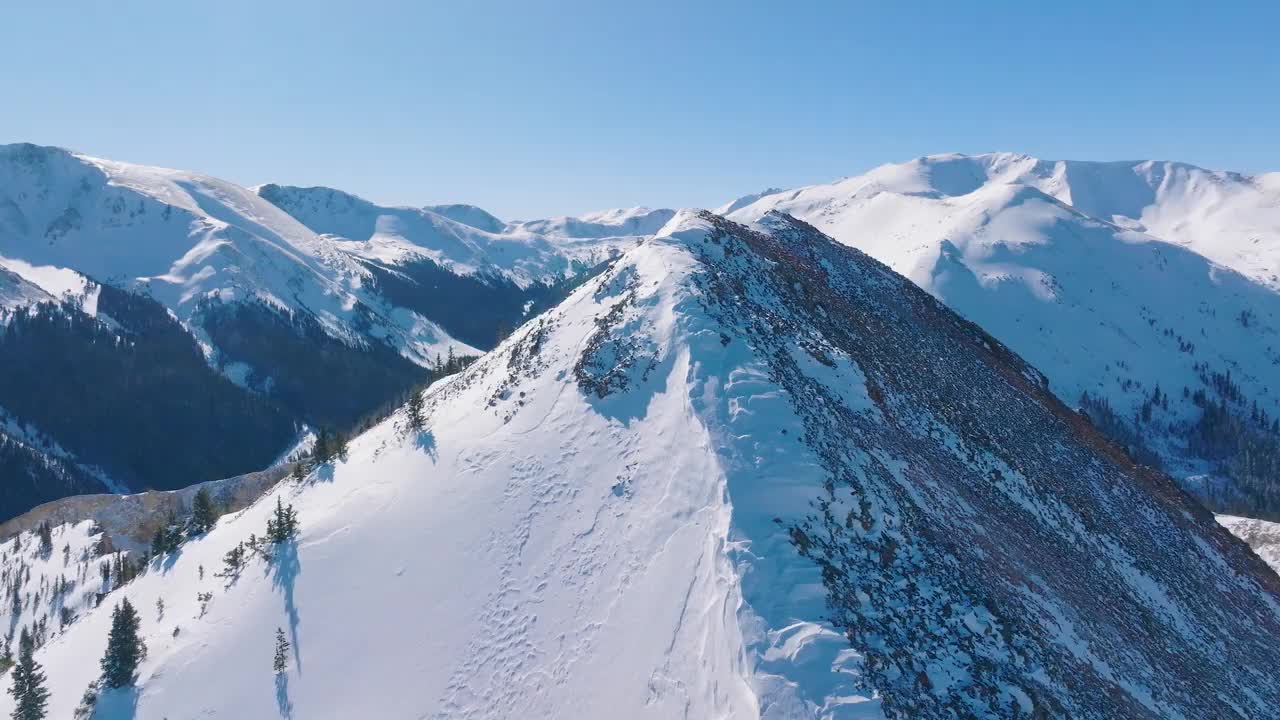 航拍视频，冬天岩石山脉被树木和明亮的雪覆盖视频素材