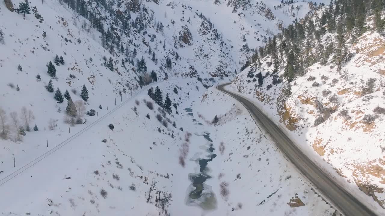 航拍的道路在岩石山脉覆盖着树木和明亮的雪在冬天视频素材