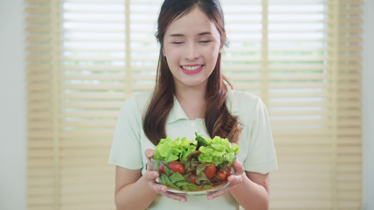 一个微笑的女人在家里的厨房里吃着新鲜的沙拉。素食视频素材