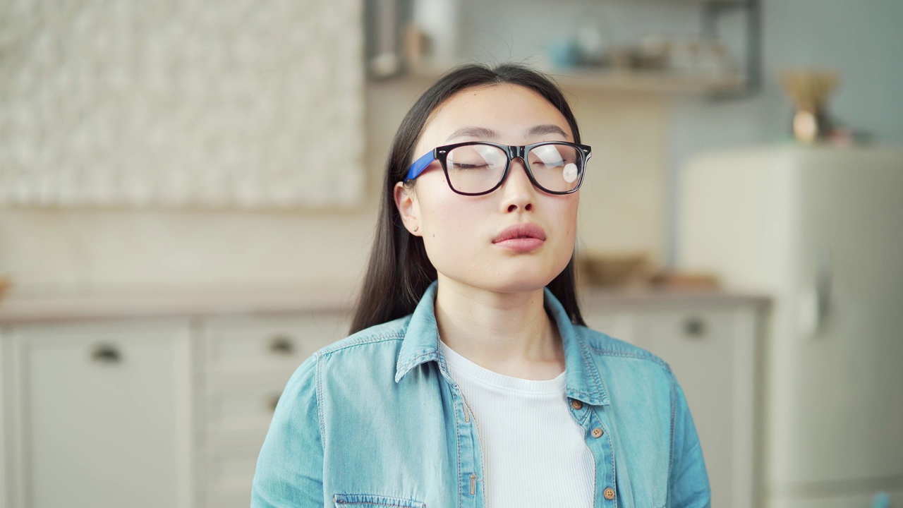 一个年轻的亚洲女人闭着眼睛坐在客厅里冥想的特写。视频素材