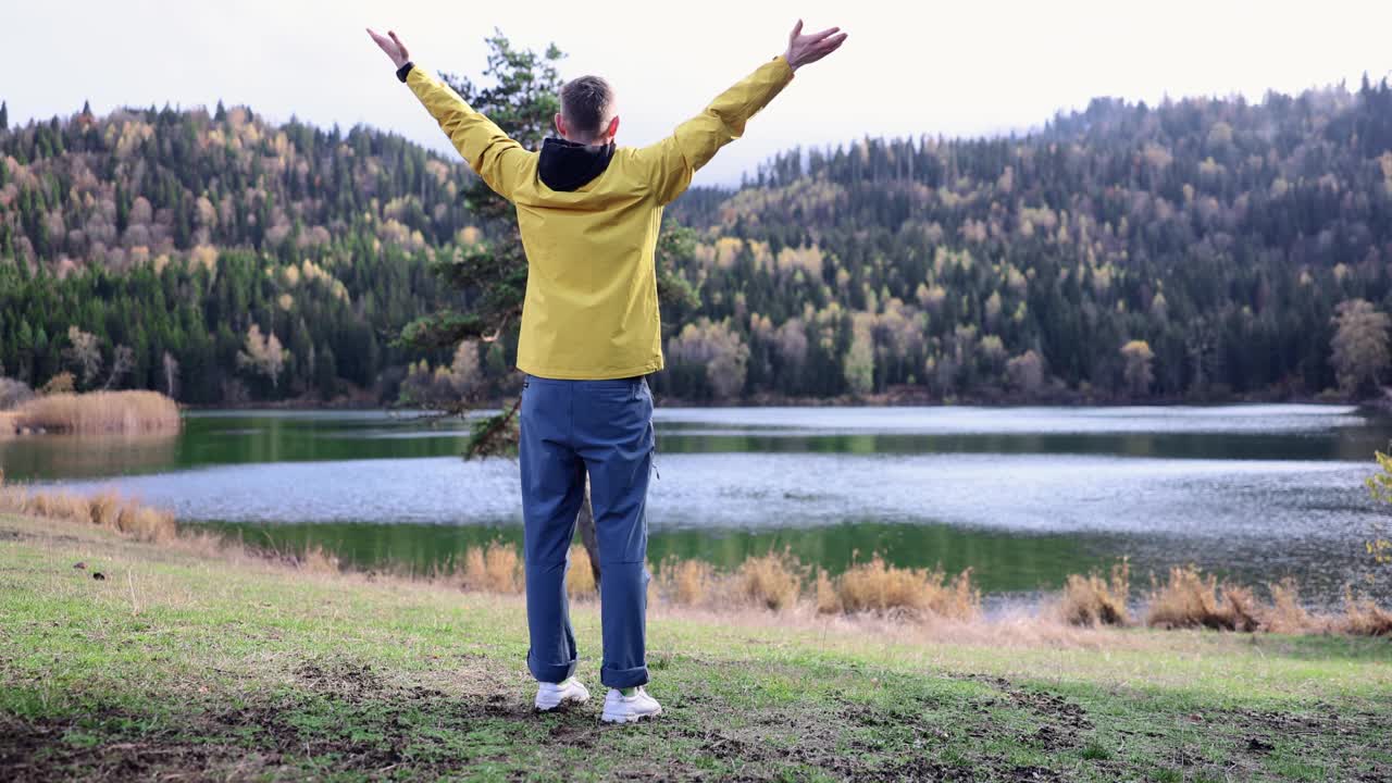 在国家公园的湖边，一名男性徒步旅行者举起双手，看起来很开心视频素材