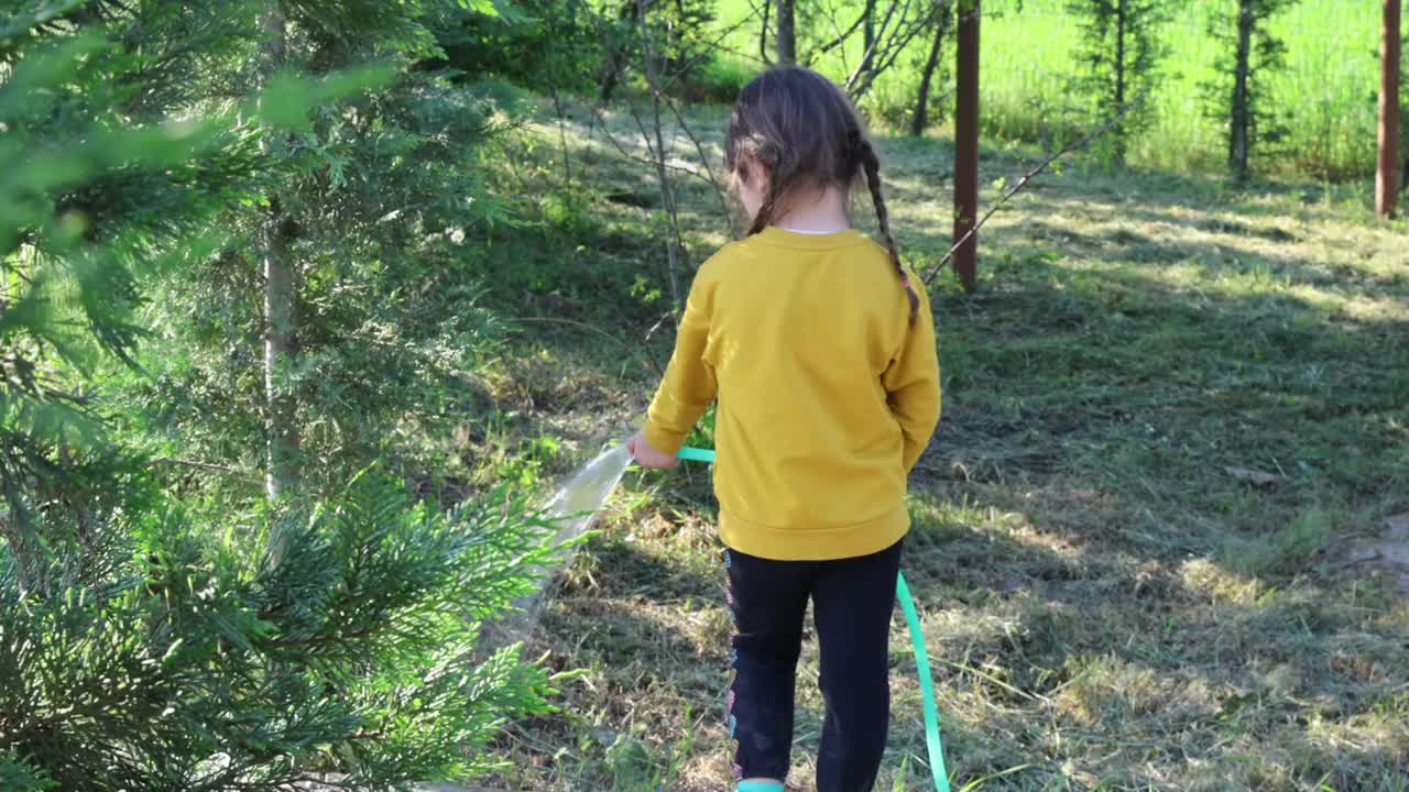 小女孩在花园里用水管给花草树木浇水视频素材