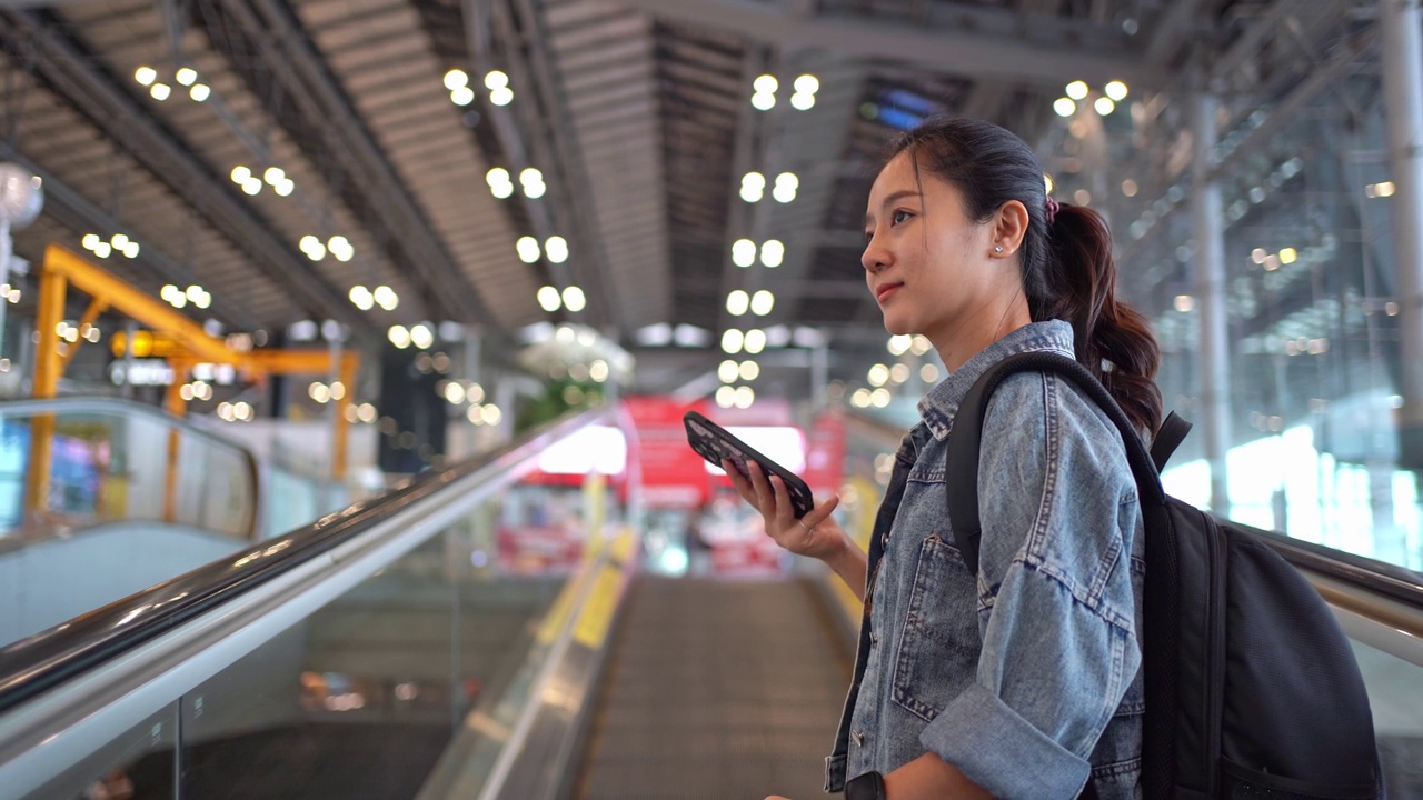 亚洲女性旅客在机场使用智能手机。她正在使用自动扶梯。视频素材