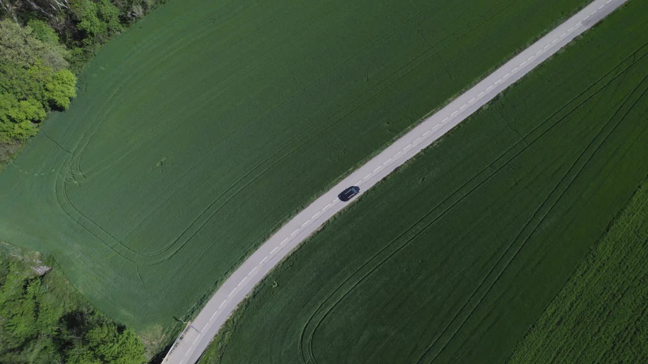 被绿色田野包围的道路上行驶的汽车，由无人机拍摄视频下载