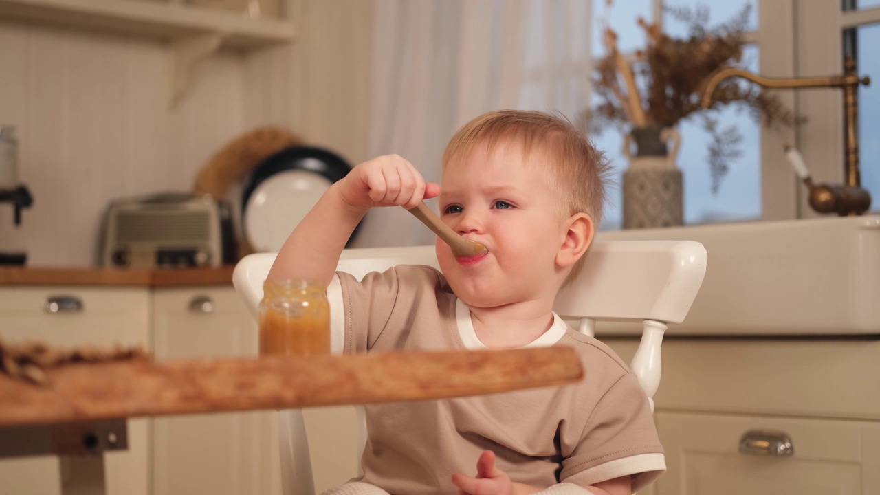 家庭美满。小男孩在厨房里自己吃东西。小男孩的凌乱滑稽的脸吃健康食品。孩子学会拿着勺子自己吃东西。自我喂养。视频素材