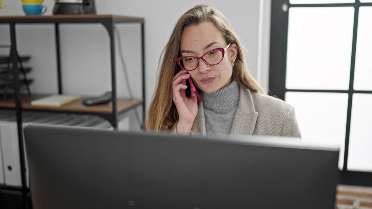 年轻的白人女性商务工作者在办公室用智能手机与电脑交谈视频素材