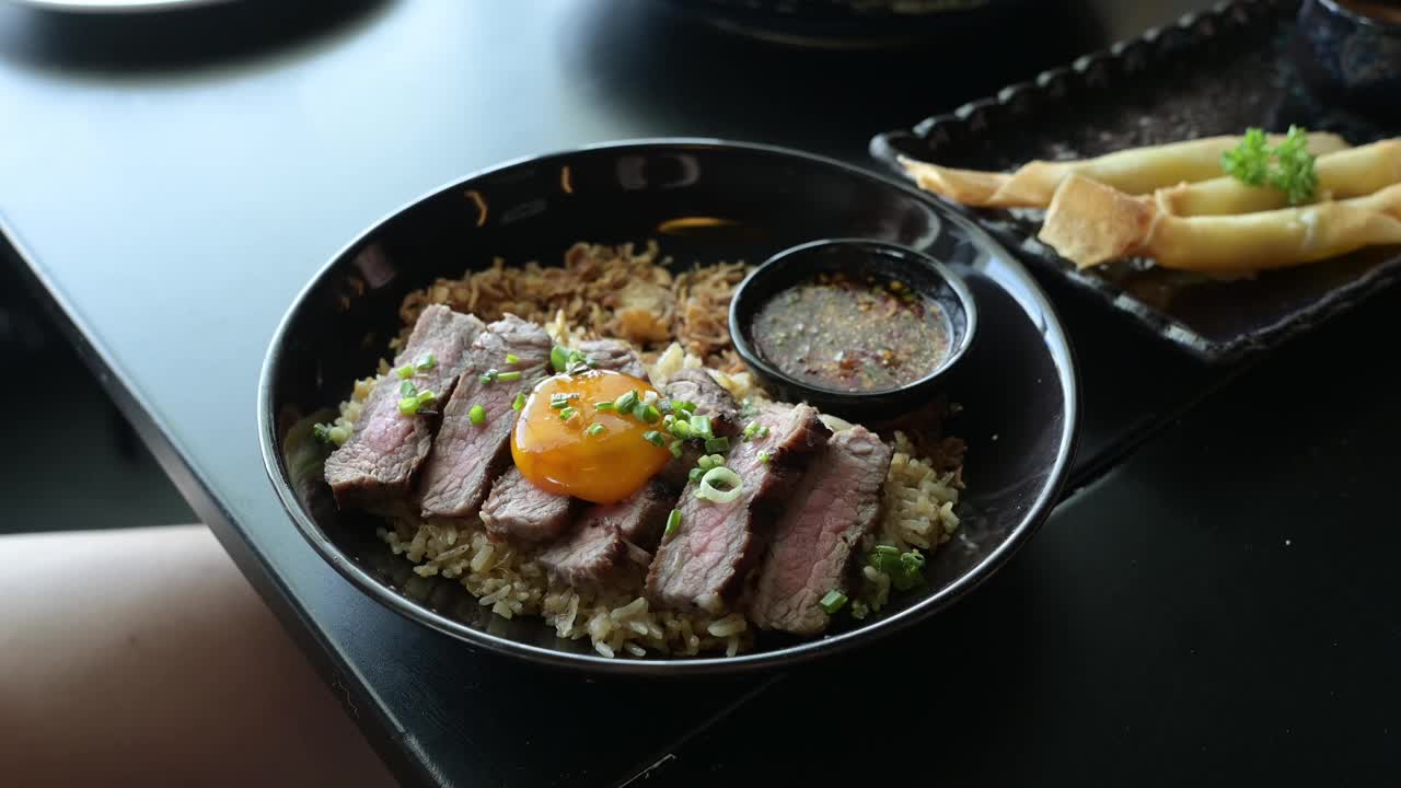 牛油蒜炒饭配牛排，配上腌蛋黄，放在木桌上的碗里。烤肉，泰国菜是一种融合的食物。视频素材