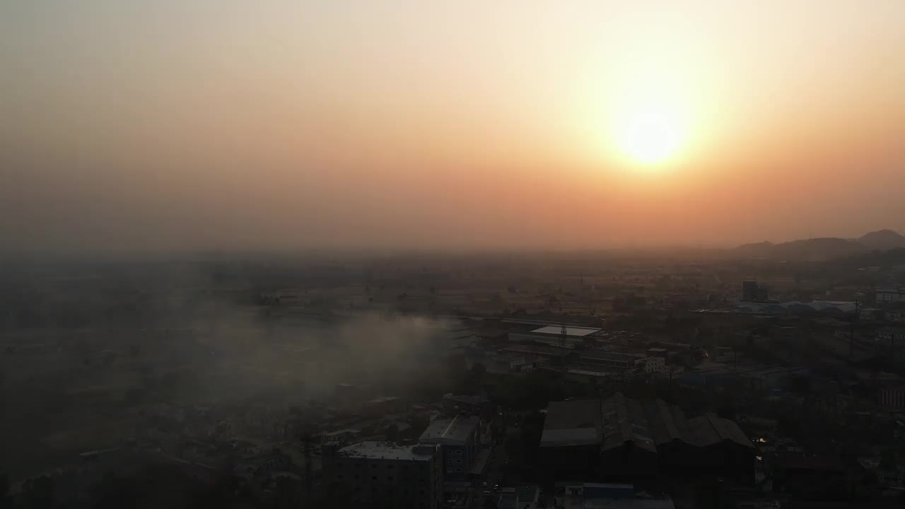 无人机在烟雾弥漫的天空中拍摄的城市景观，地平线上是橙色的日落天空视频素材