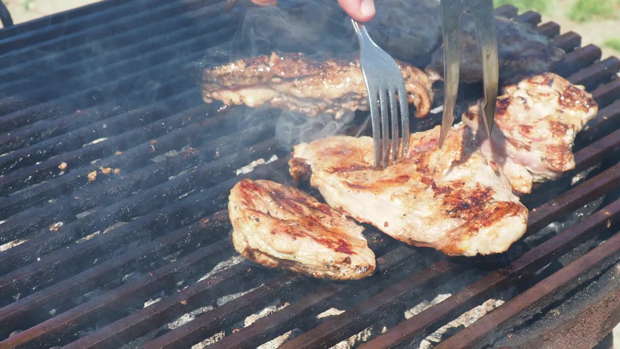 烧烤师傅检查肉的熟度。烤多汁的肉，猪肉牛排，在烧烤架上燃烧的煤，火焰和烟雾。烤多汁条纹牛排。肉汁喷涌而出，嘶嘶作响。视频素材