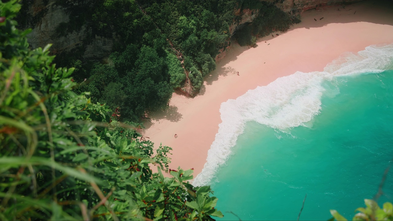 热带海滩，光滑的粉色沙滩和迷人的蔚蓝海浪。俯瞰美丽的海景，海岸线上有绿色的雨林。视频素材