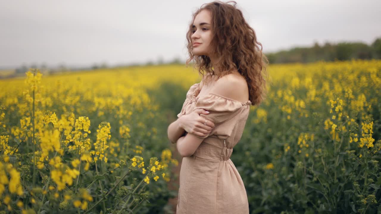 一个微笑的女人站在户外的菜地里。一个风骚的卷发女孩甜甜地笑着。一个年轻女子在夏日盛开的田野里自由自在的特写。视频素材