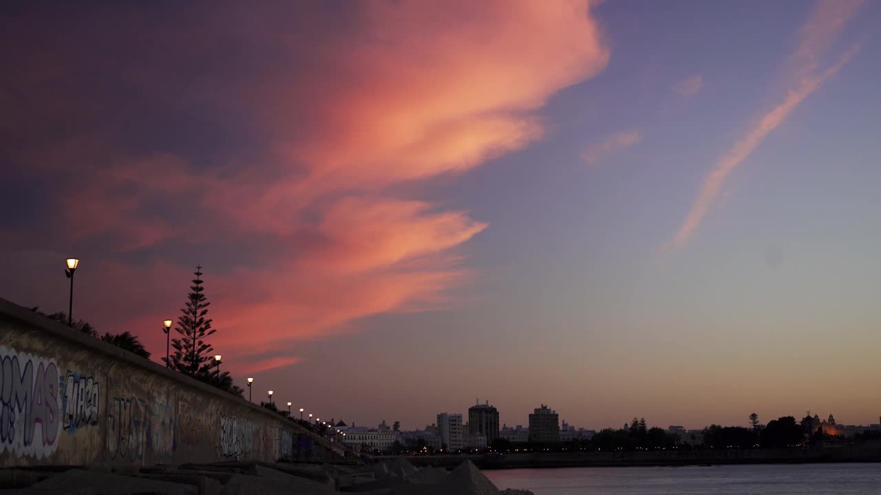 晚上日落。粉红色的云飘过蓝天。背景是城市。落日在湖面上的倒影。美丽landscape.4К视频素材