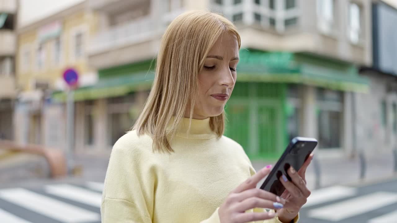 年轻的金发女子在街上用着智能手机，表情严肃视频素材