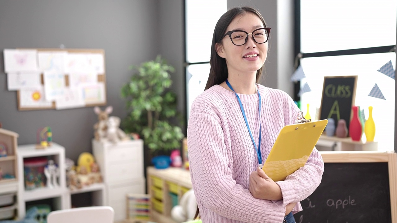 年轻的中国女幼儿园老师微笑着自信地拿着写字板视频素材