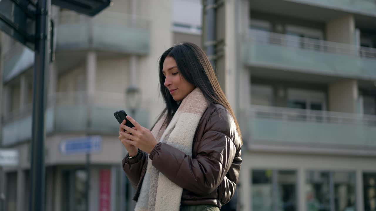 一位年轻女子站在城市街道上看智能手机。在城市环境中通过电话收到积极通知的人视频素材