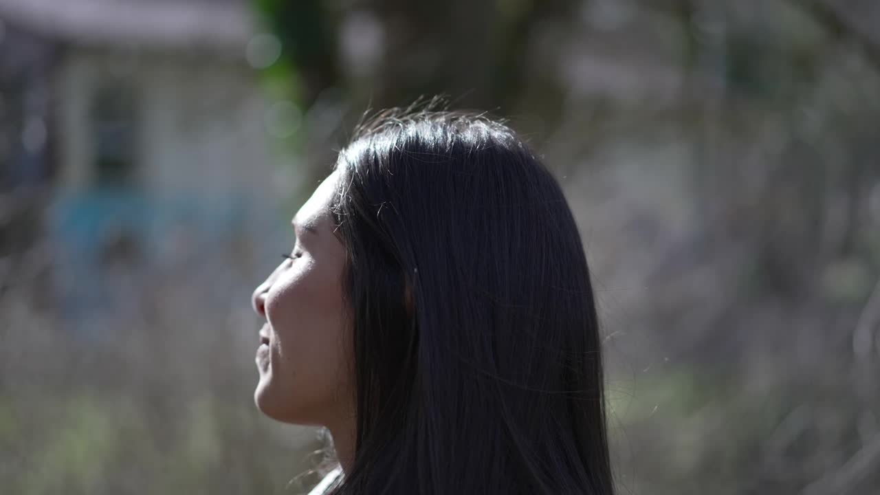 侧面特写，一个沉思的年轻黑发女子走在公园外面，感到满足和喜悦视频素材