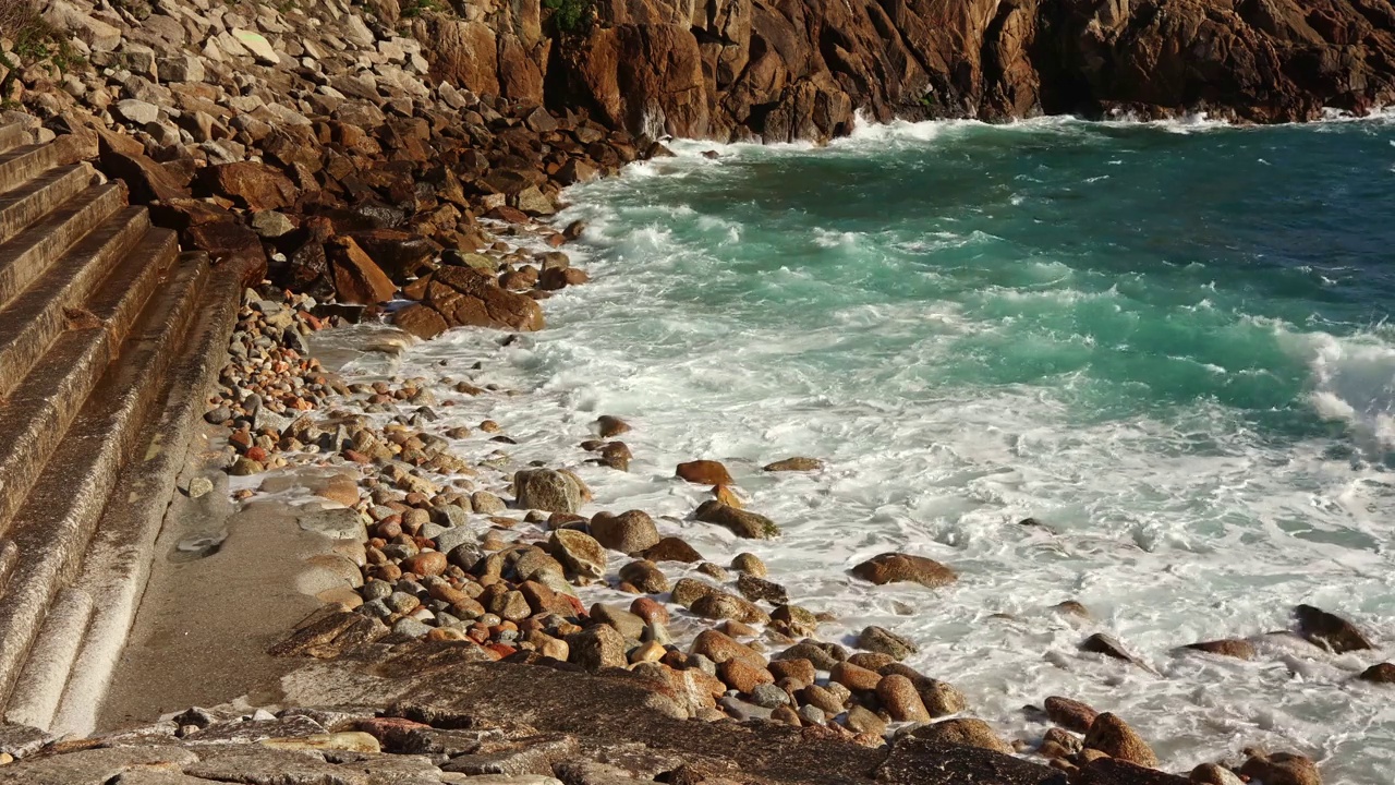 碧绿的海水，在阳光明媚的夏天，海浪拍打着石头海岸。视频素材