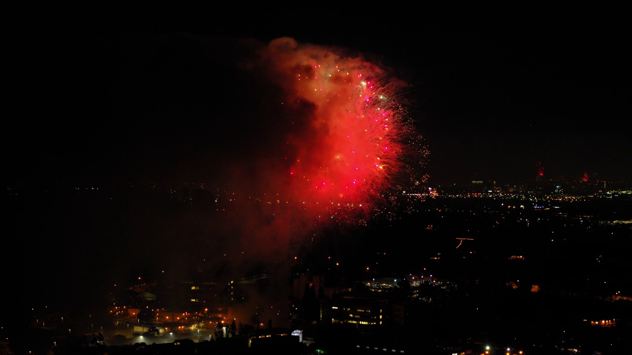 空中拍摄的烟花在城市郊区对着天空爆炸，无人机在夜晚飞过灯火通明的城市景观-洛杉矶，加利福尼亚视频素材