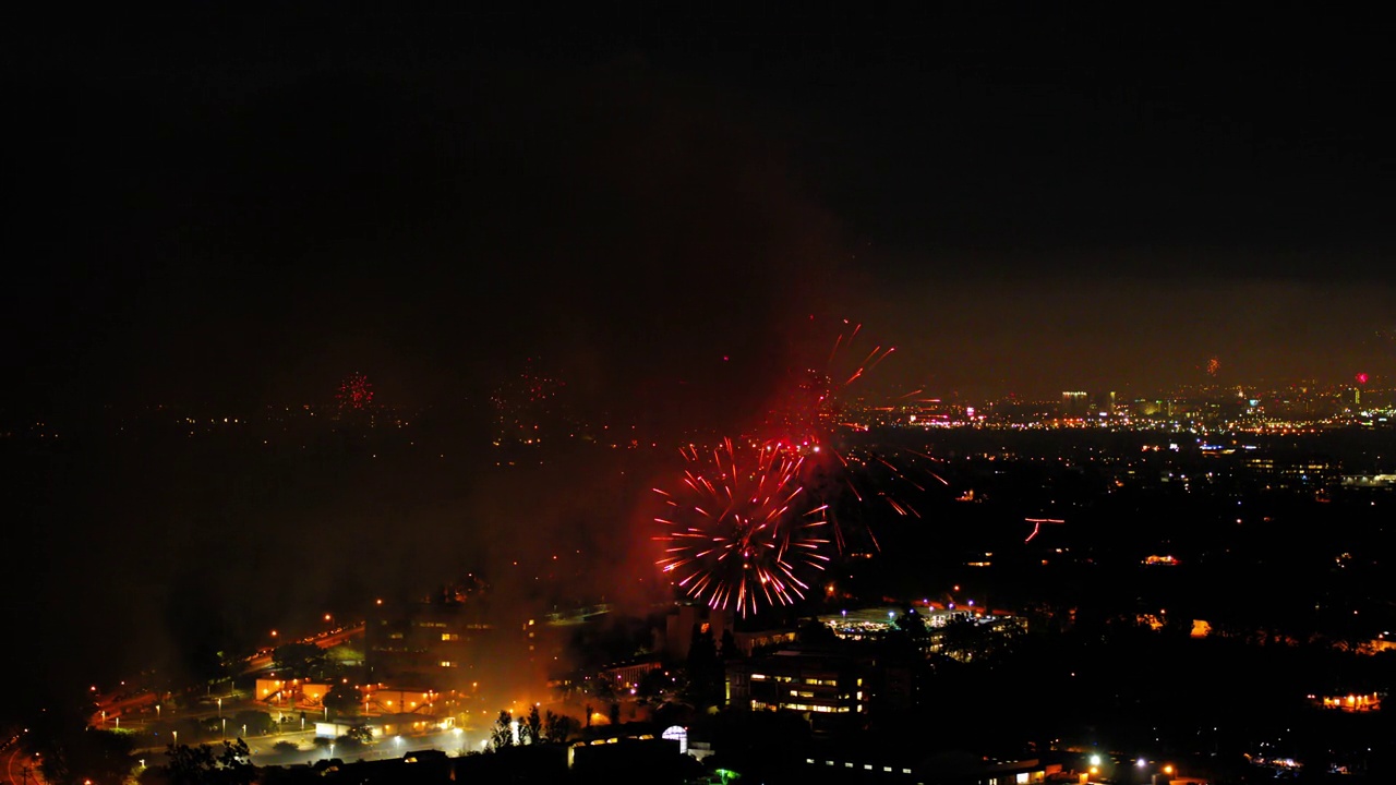 空中拍摄的烟花在城市郊区对着天空爆炸，无人机在夜晚飞过灯火通明的城市景观-洛杉矶，加利福尼亚视频素材