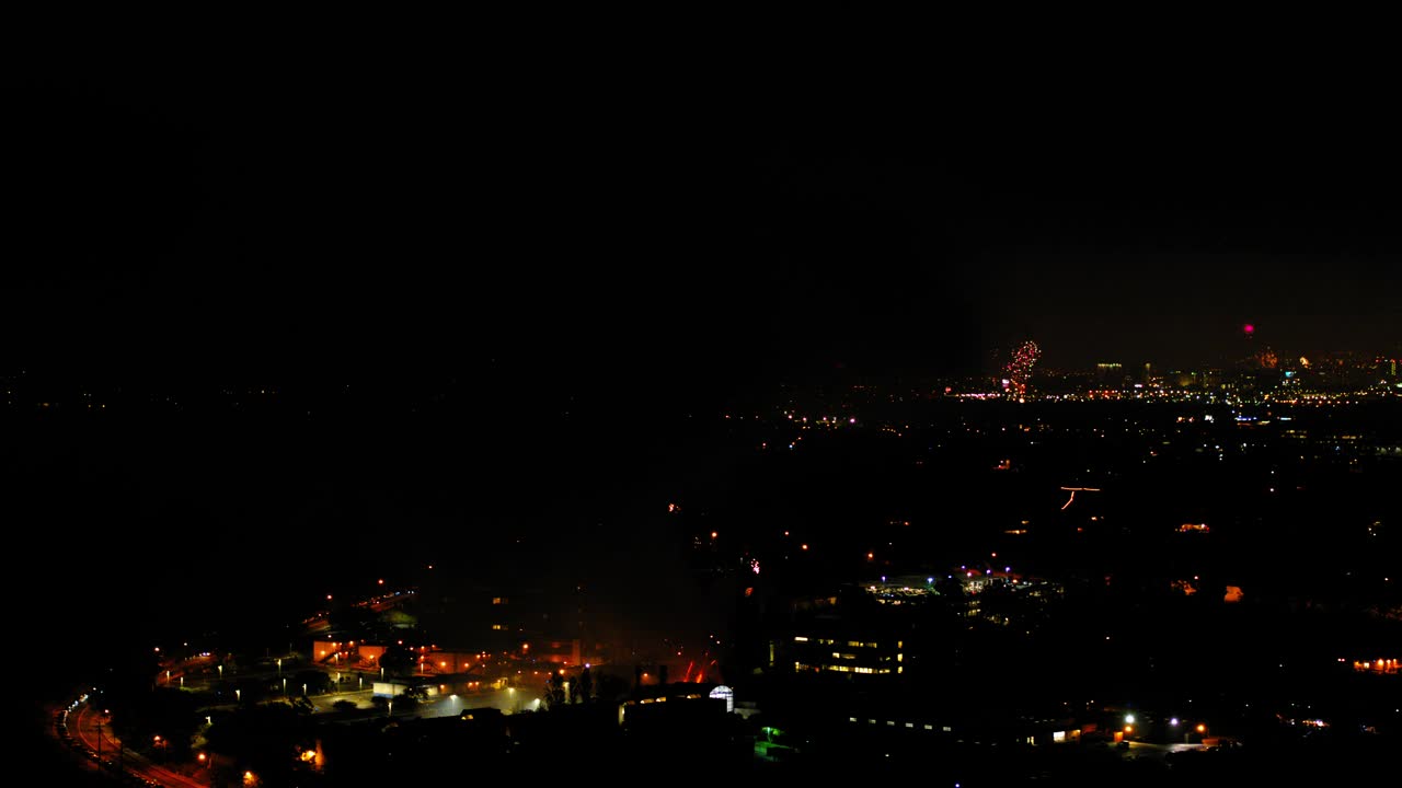 空中平移拍摄的烟花在城市郊区对着天空爆炸，无人机在夜晚飞过灯火通明的城市景观-洛杉矶，加利福尼亚视频素材