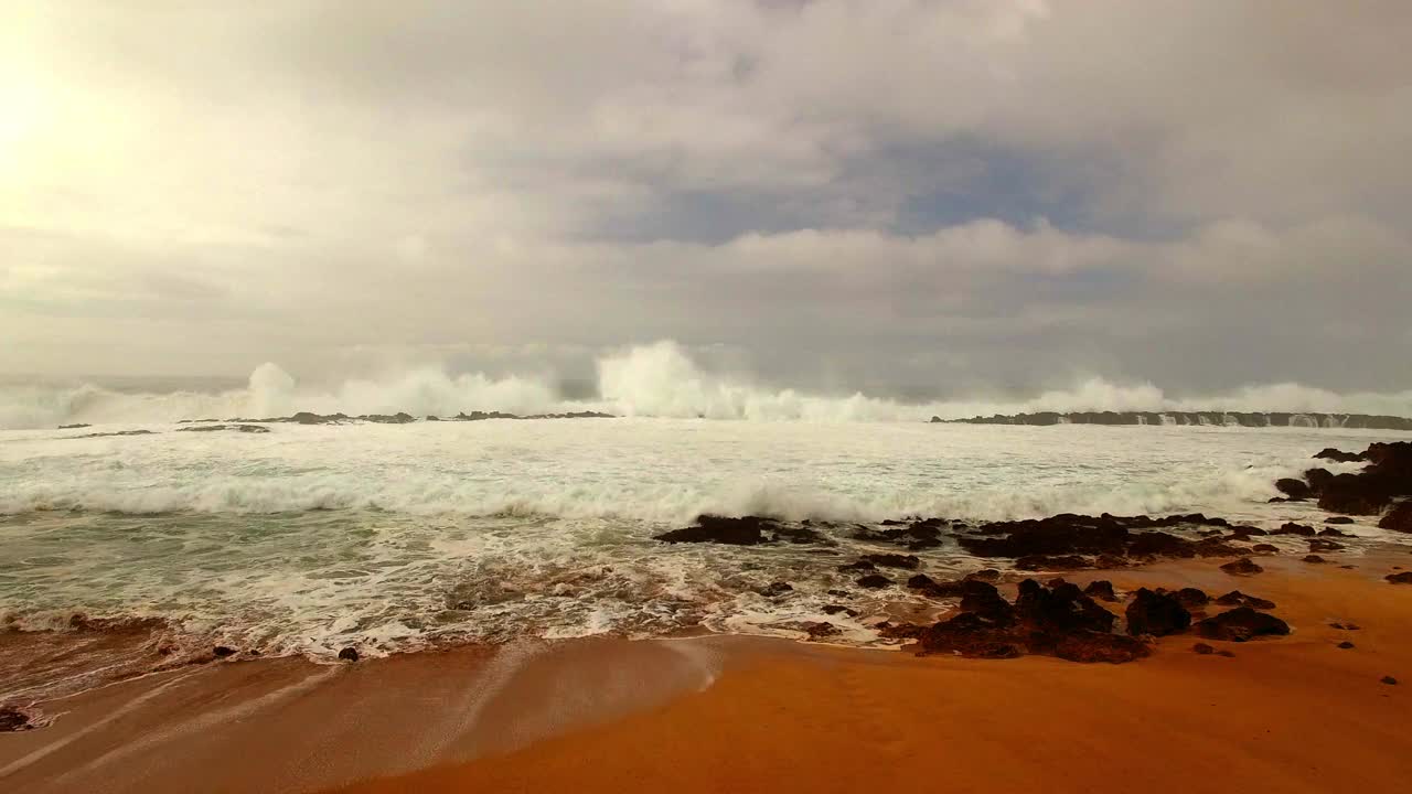 航拍:无人机向前飞行的海浪溅在海岸上的海滩上对多云的天空-夏威夷瓦胡岛视频素材