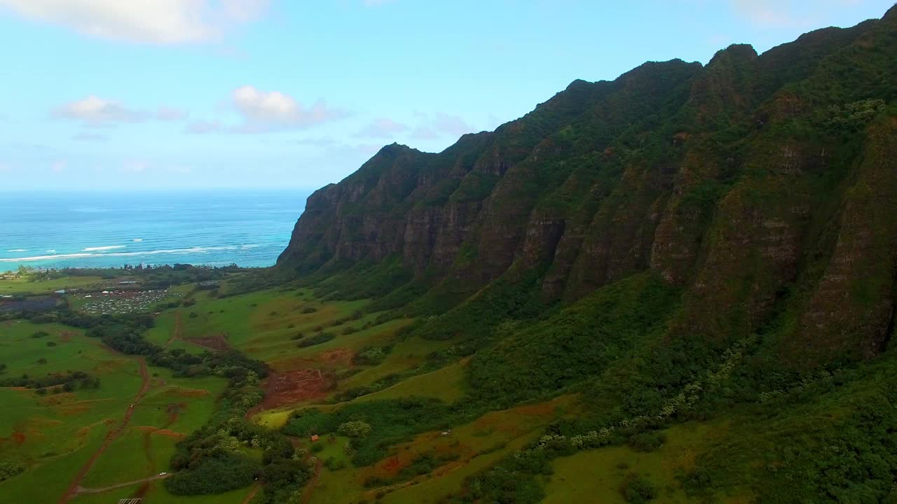 在夏威夷瓦胡岛，无人机在绿色景观上向后飞行，航拍的靠近大海的山与蓝天视频素材