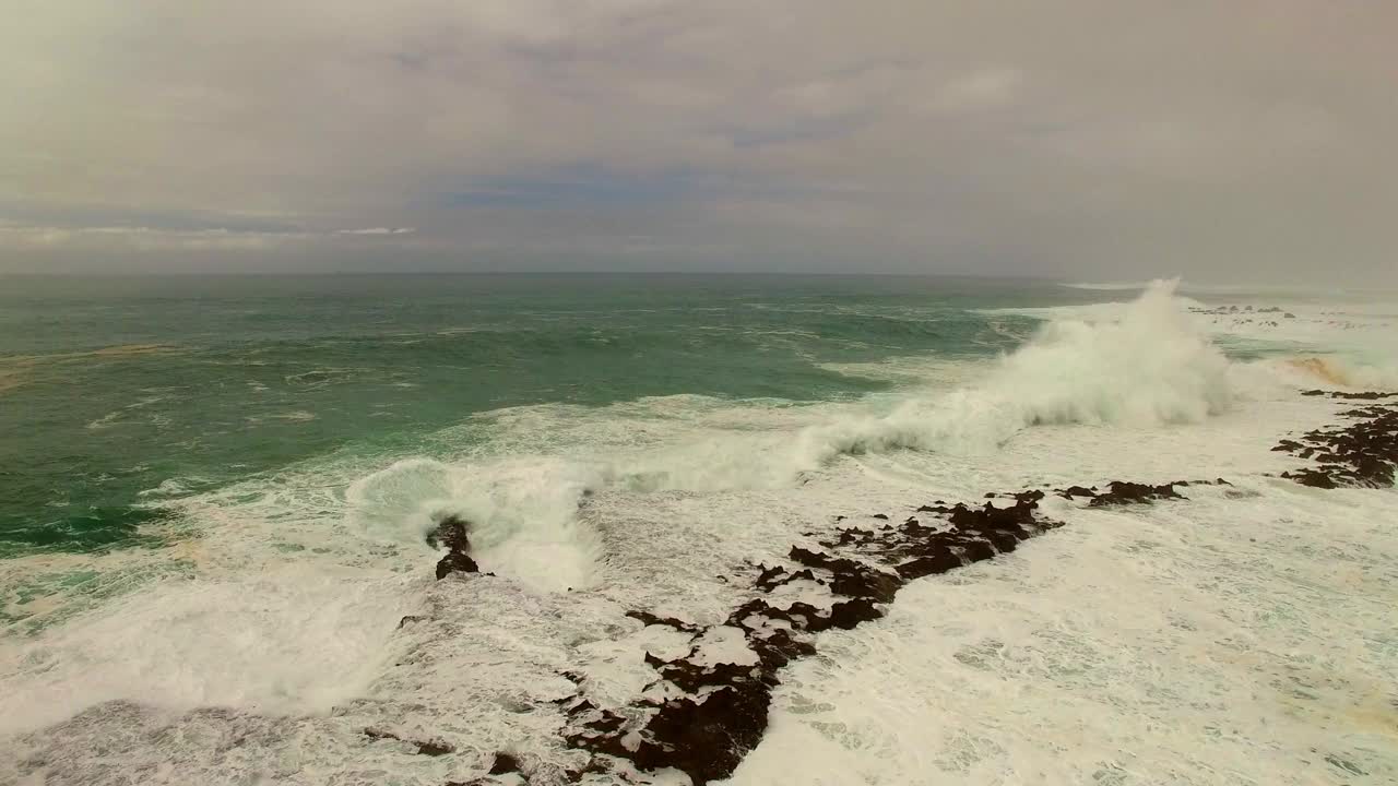 航拍:无人机飞越海浪溅在岩石上，在海上对多云的天空在日落-瓦胡岛，夏威夷视频素材