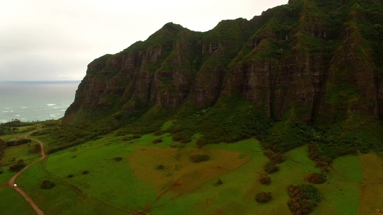 航拍的车辆在土路附近的山和海，无人机飞行在绿色景观在日落-瓦胡岛，夏威夷视频素材