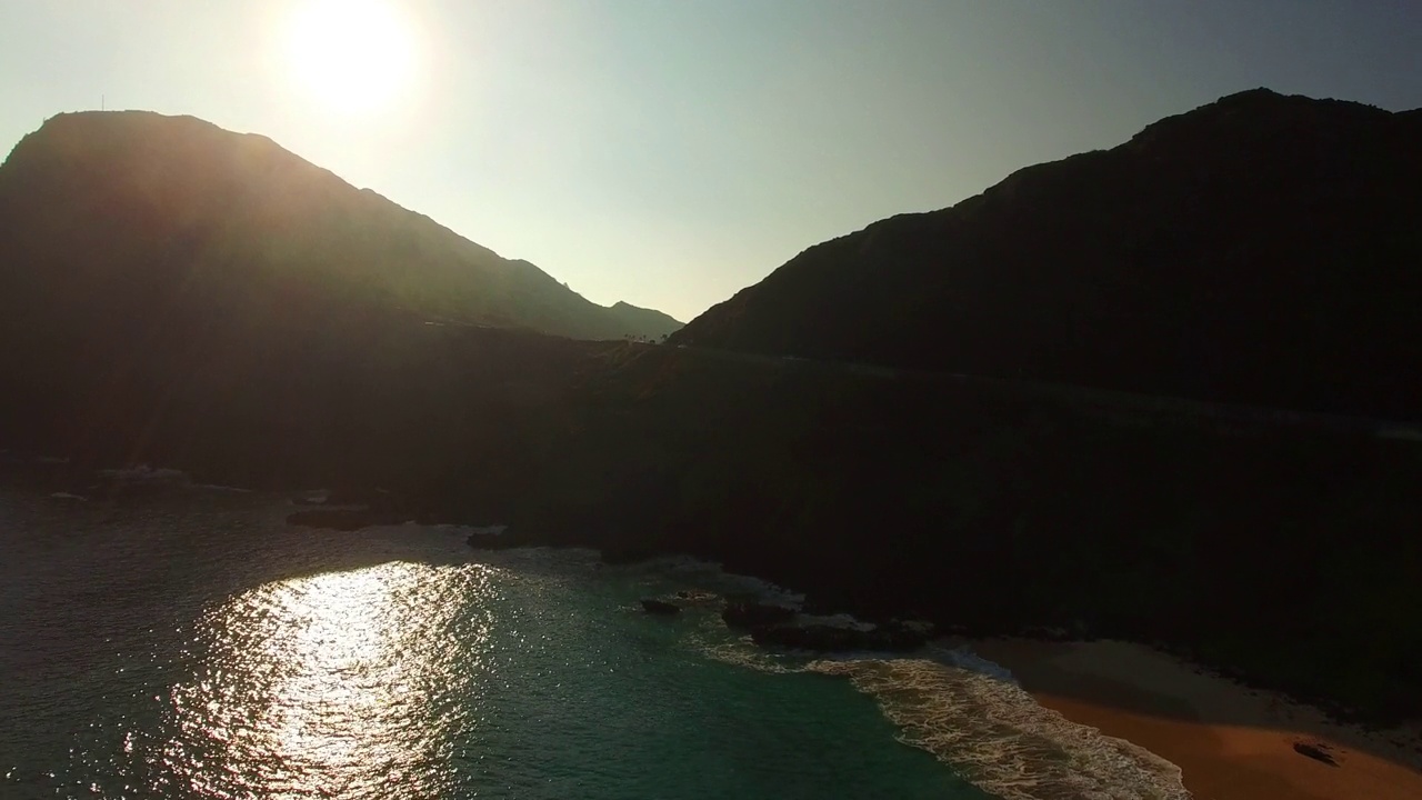 空中平移拍摄的海上山与车辆在道路上，无人机飞行在海岸线对天空在日落-瓦胡岛，夏威夷视频素材