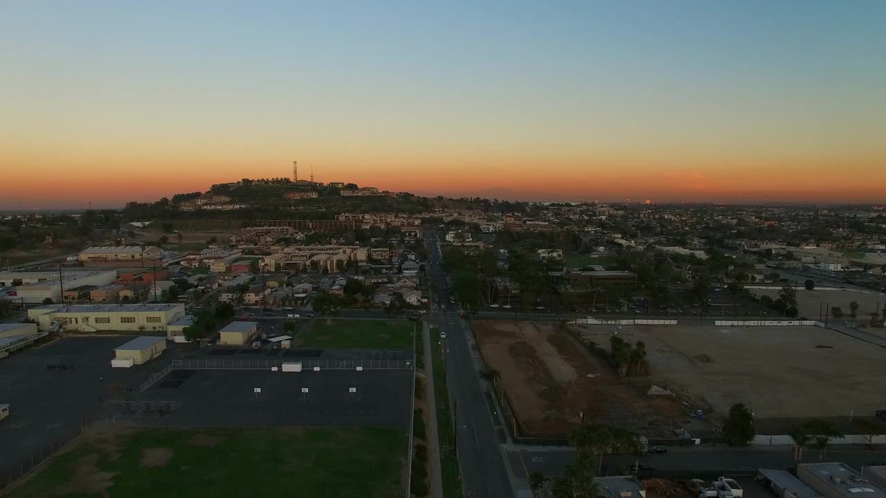 黄昏时分，在橙色天空的衬托下，无人机在城市附近飞行，加州长滩视频素材