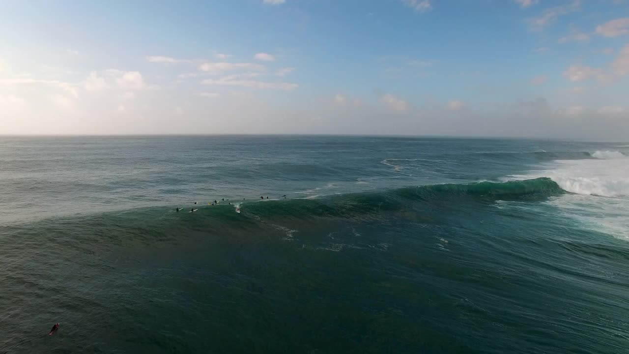 空中倾斜拍摄的人们在海浪上冲浪对天空，无人机在海上飞行在日落-瓦胡岛，夏威夷视频素材