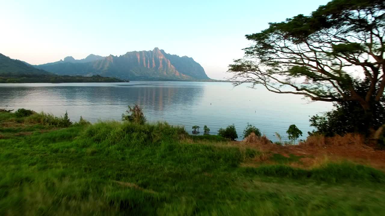 在日落时，无人机在海岸线前飞行，在夏威夷瓦胡岛附近的山脉对天空的航拍视频素材