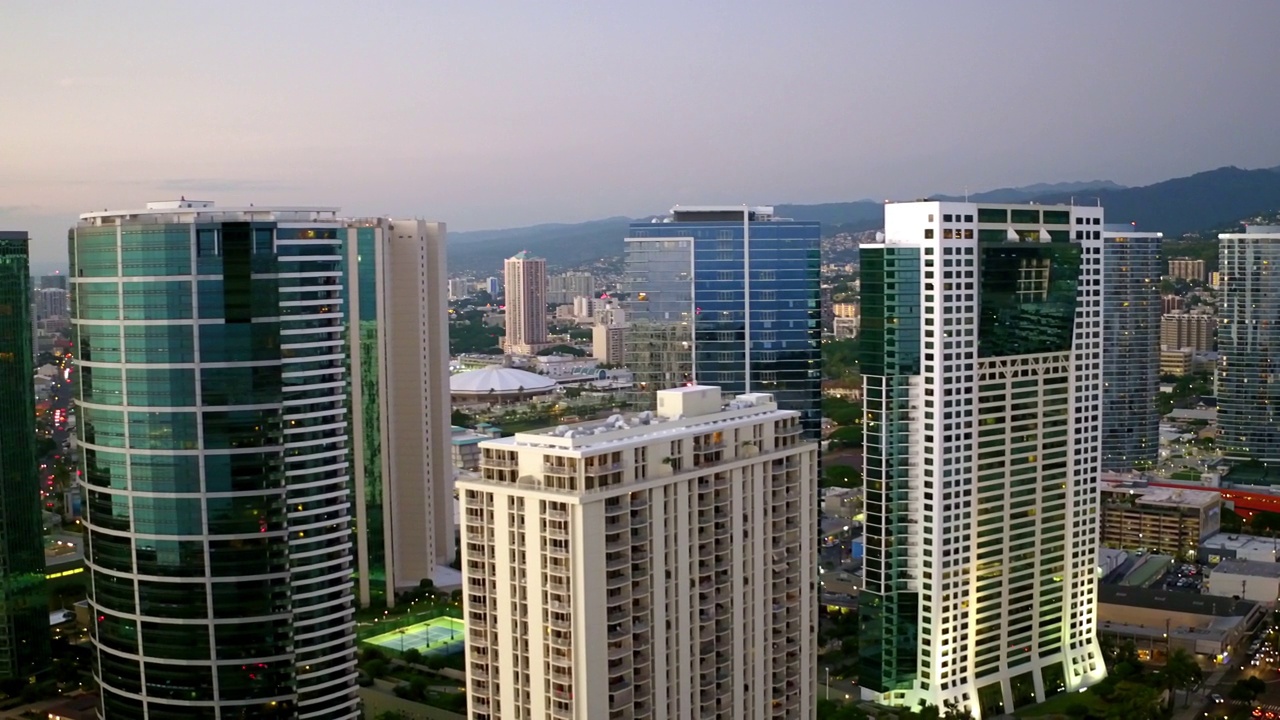 日落时分，无人机在夏威夷瓦胡岛的城市景观上飞行，对城市中现代建筑的空中平移拍摄视频素材