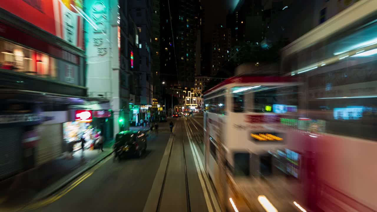 在香港岛中心沿道路行驶的有轨电车前方拍摄的动态延时镜头。有轨电车晚上在香港金融区运行，接送乘客视频下载