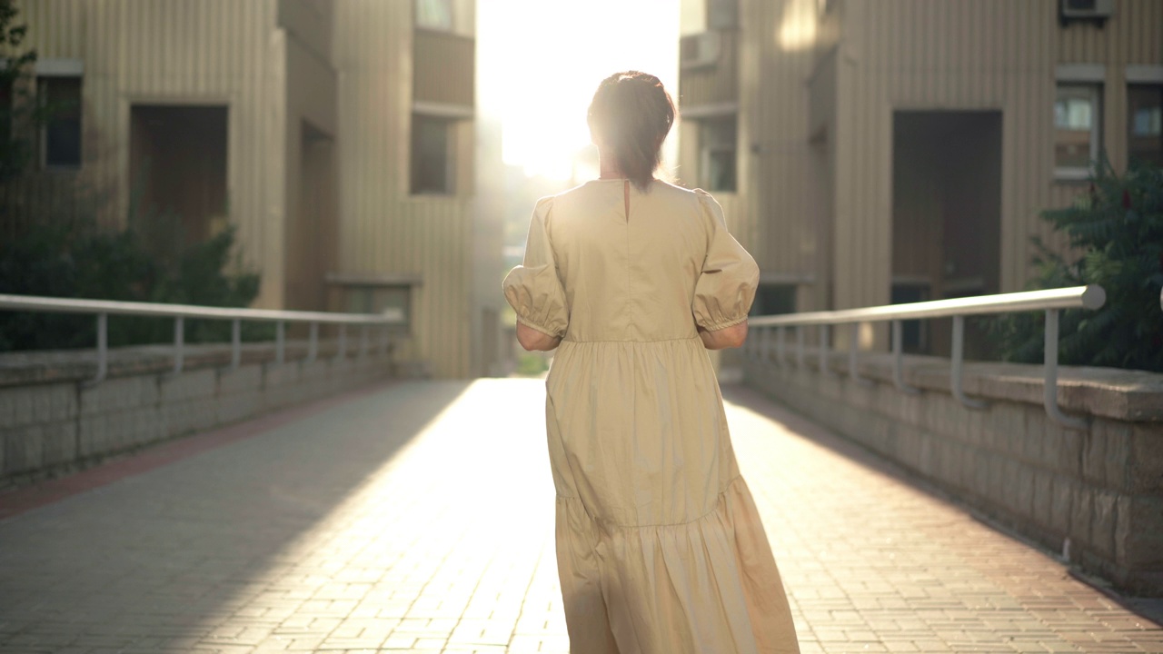 夕阳下，成熟女子在城市街道的阳光下行走的跟踪镜头。白种女性退休人员日落时在阳光下散步的背影。视频素材