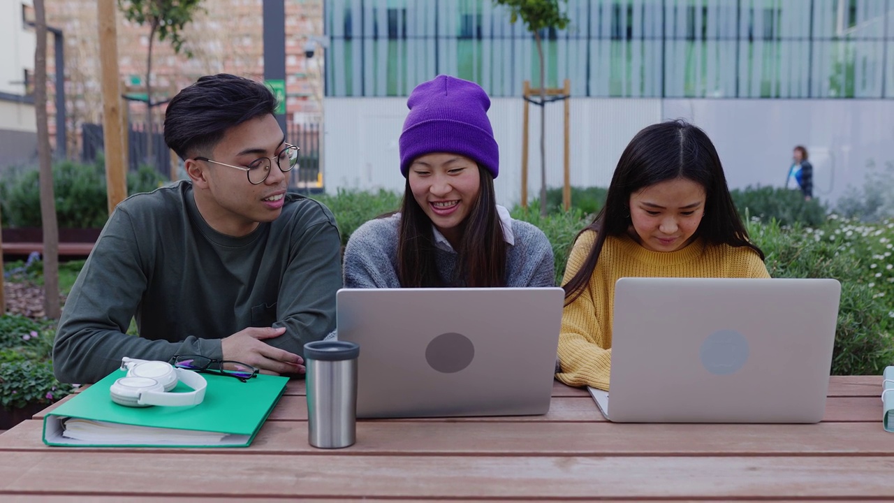 三个年轻的亚洲学生朋友在桌子大学校园里一起学习。视频素材