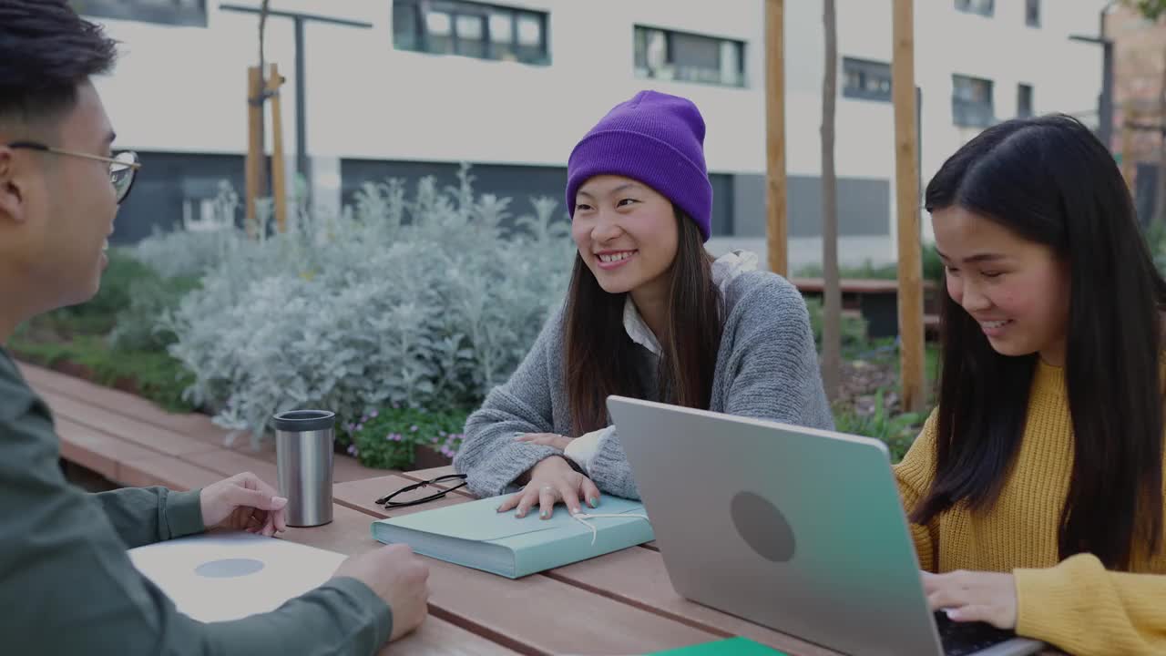 三个年轻的学生朋友在户外学习时谈笑风生。视频素材