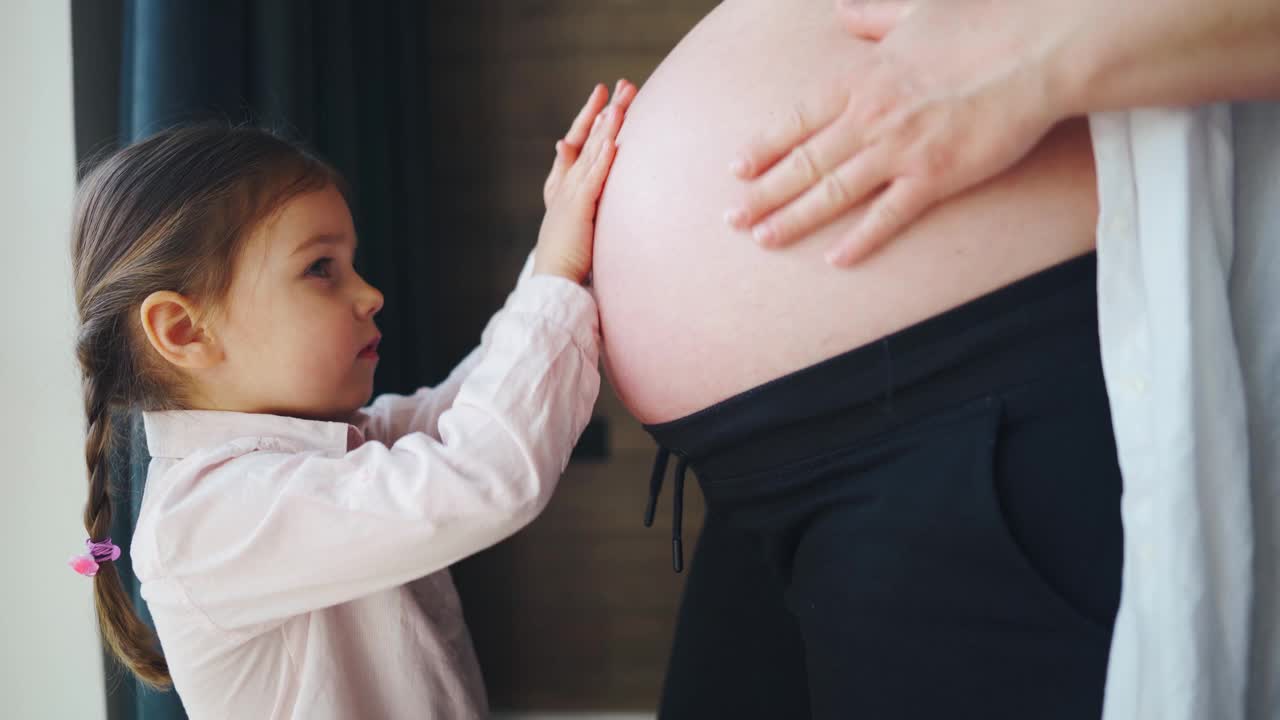 可爱的小女孩抚摸并亲吻怀孕妈妈的肚子。妊娠、新生儿视频素材