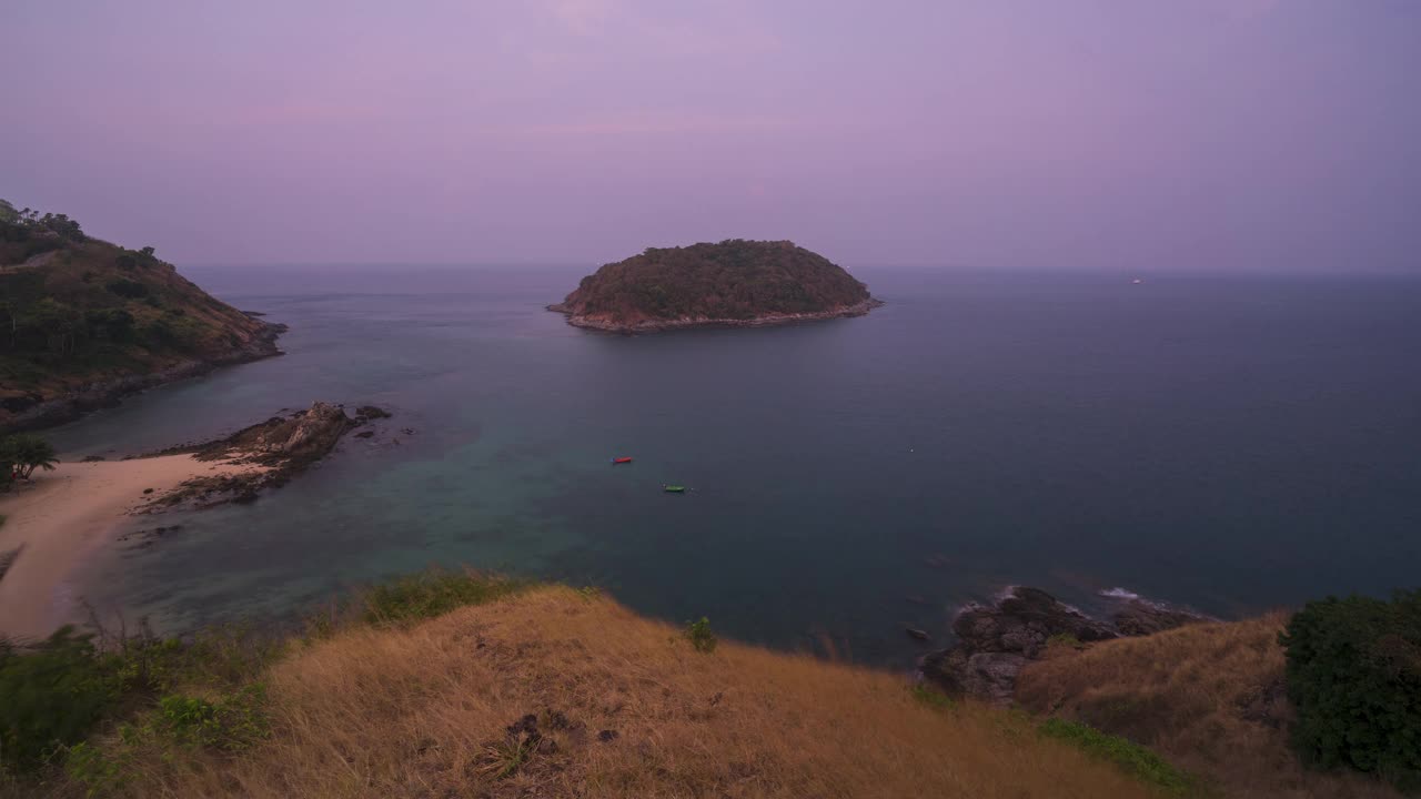 在泰国普吉岛的雅伊海滩，晨光照射在大海中央的山脉和黄色的草地上。视频下载