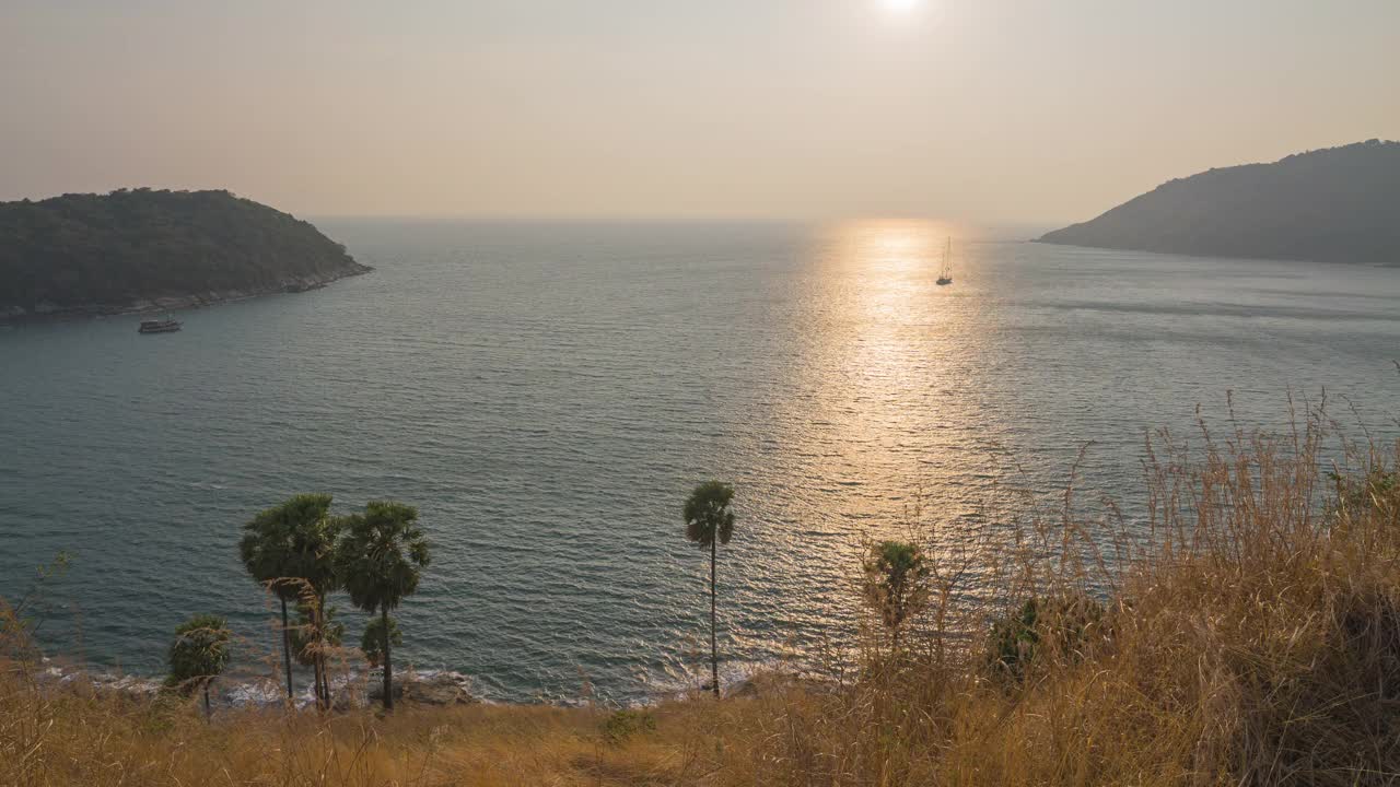 在泰国普吉岛的雅伊海滩，晨光照射在大海中央的山脉和黄色的草地上。日落视频下载