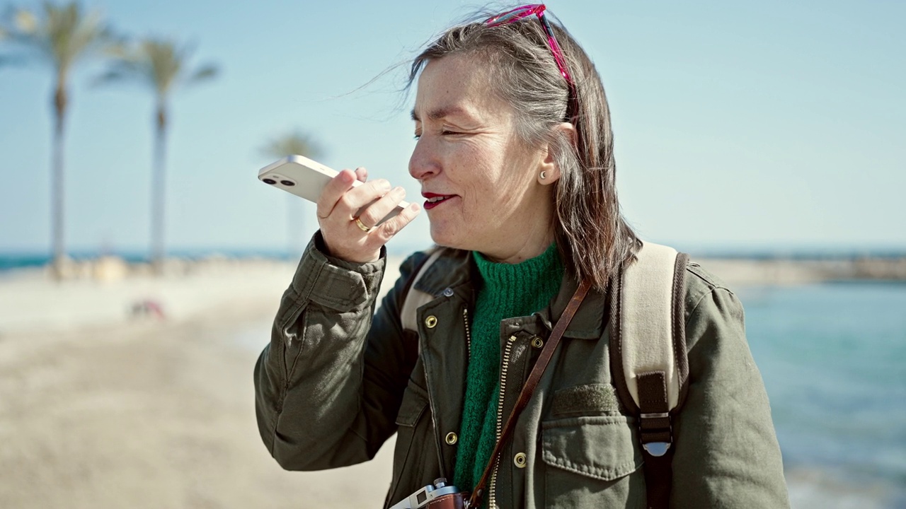 一个白发的西班牙裔成熟女人背着背包在海边打电话视频素材