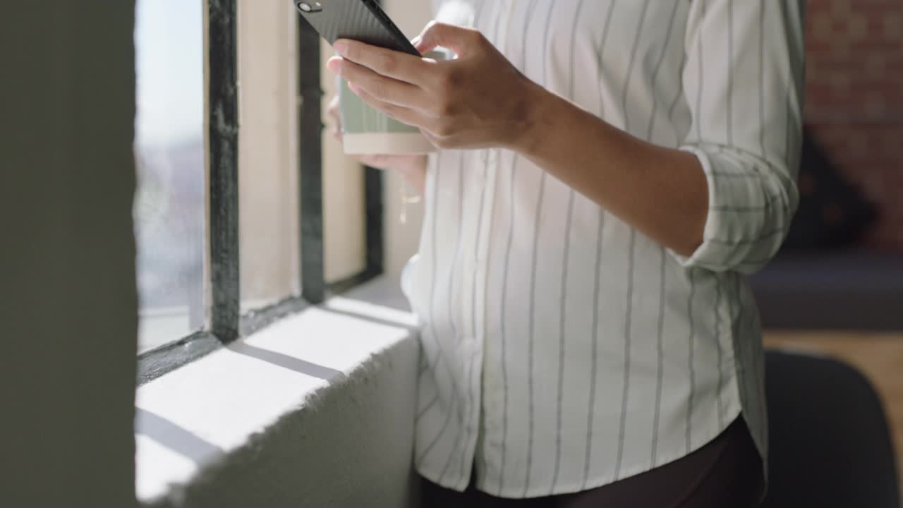 美丽的西班牙女性在家里用智能手机喝咖啡，享受轻松的早晨，浏览信息，看着窗外沉思视频素材