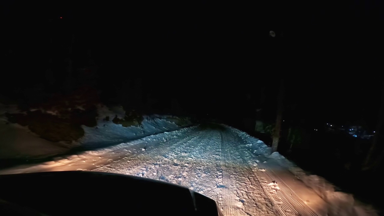 一辆带着前灯的汽车在夜晚滑滑的雪山路上行驶视频素材